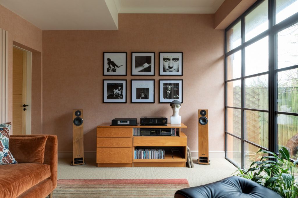 Contemporary listening room with high-end audio system, wooden media unit, floorstanding speakers, framed artwork, and large industrial-style windows.