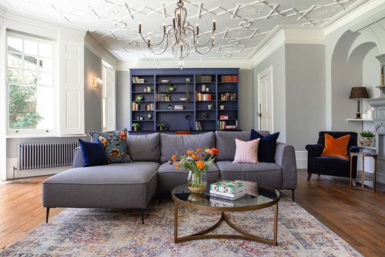 Elegant living room with bespoke blue shelving, statement chandelier and grey sectional sofa.